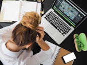Overhead view of a stressed woman working at a desk with a laptop, phone, and notebooks.